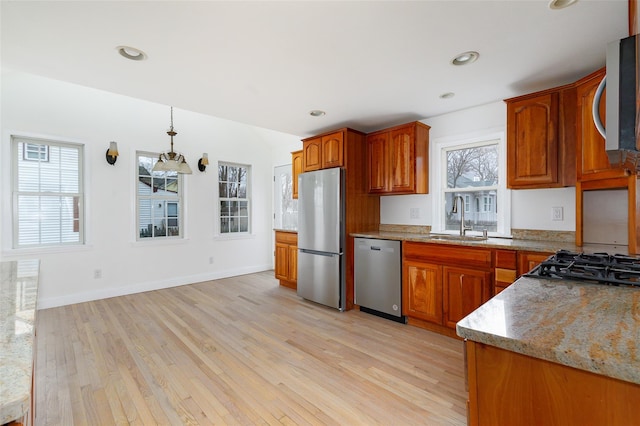 kitchen featuring pendant lighting, sink, light stone countertops, appliances with stainless steel finishes, and light hardwood / wood-style floors