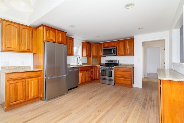 kitchen with light stone counters, light hardwood / wood-style flooring, sink, and appliances with stainless steel finishes