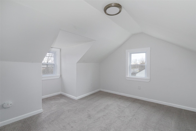 additional living space featuring light colored carpet, a healthy amount of sunlight, and vaulted ceiling