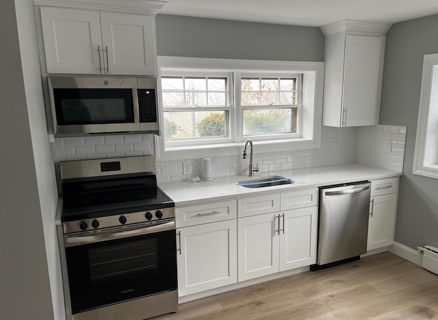 kitchen featuring light wood finished floors, stainless steel appliances, light countertops, white cabinets, and a sink