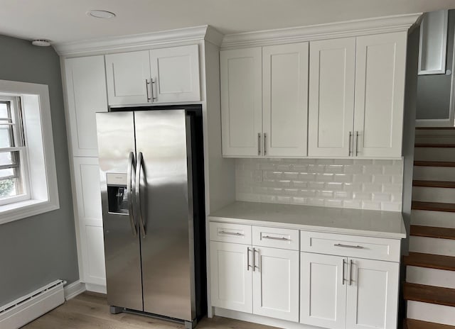 kitchen with a baseboard radiator, light wood-style flooring, decorative backsplash, white cabinets, and stainless steel fridge