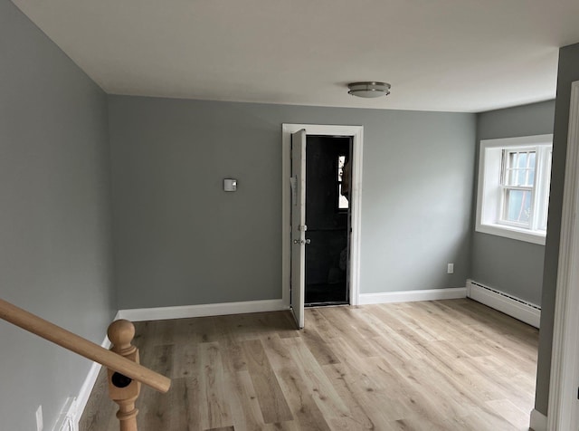 unfurnished room with a baseboard radiator, light wood-style flooring, and baseboards