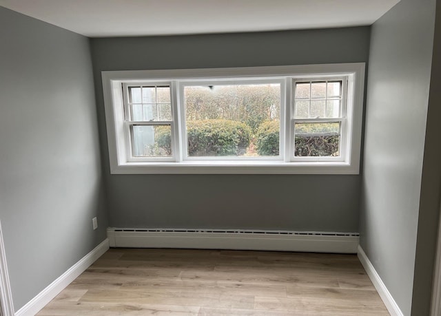 empty room with light wood-style floors, a baseboard radiator, and baseboards