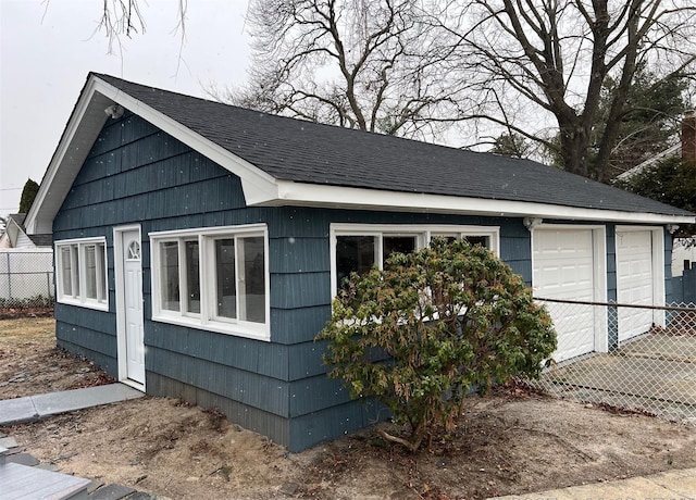 view of property exterior featuring an outbuilding, a shingled roof, fence, and a garage