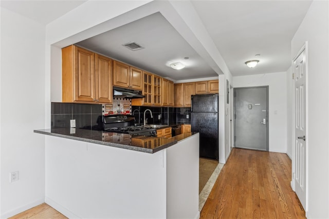 kitchen featuring kitchen peninsula, dark stone counters, black appliances, light hardwood / wood-style flooring, and sink