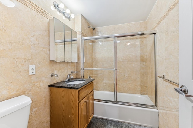 full bathroom with tile walls, shower / bath combination with glass door, vanity, and toilet