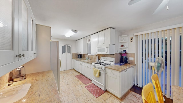 kitchen with sink, white appliances, white cabinetry, backsplash, and light stone counters