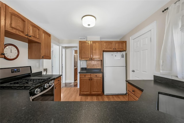 kitchen with white fridge, range with gas stovetop, and light hardwood / wood-style floors