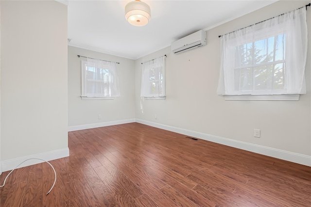 unfurnished room featuring a healthy amount of sunlight, a wall mounted AC, and wood-type flooring