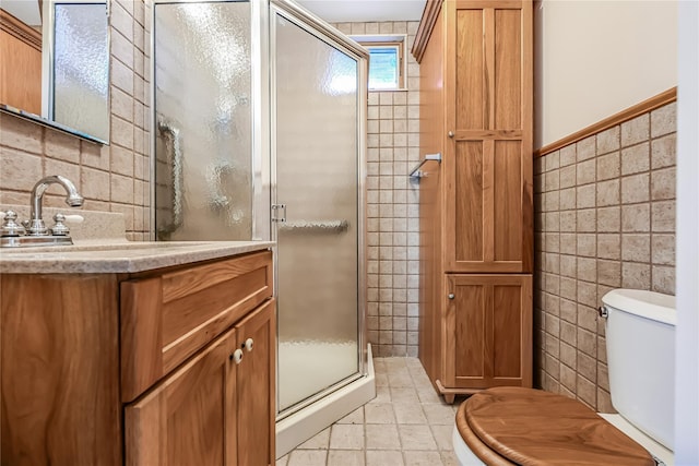 bathroom featuring toilet, vanity, tile walls, and a shower with door