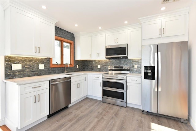 kitchen with sink, appliances with stainless steel finishes, white cabinetry, light hardwood / wood-style floors, and decorative backsplash