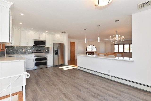 kitchen featuring decorative light fixtures, sink, white cabinets, a baseboard heating unit, and stainless steel appliances