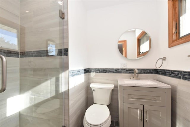 bathroom with vanity, toilet, a shower with door, and tile walls