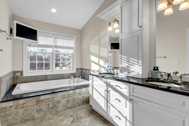 bathroom featuring vanity, tiled tub, and vaulted ceiling