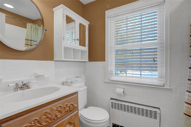 bathroom with radiator heating unit, toilet, vanity, and a wealth of natural light