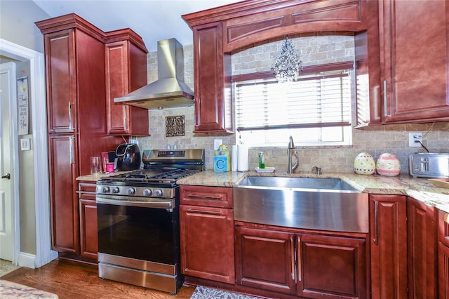 kitchen with decorative backsplash, dark wood-type flooring, gas range, wall chimney range hood, and sink