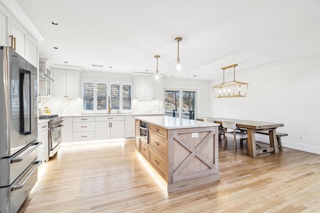 kitchen with decorative light fixtures, high quality appliances, white cabinetry, and decorative backsplash