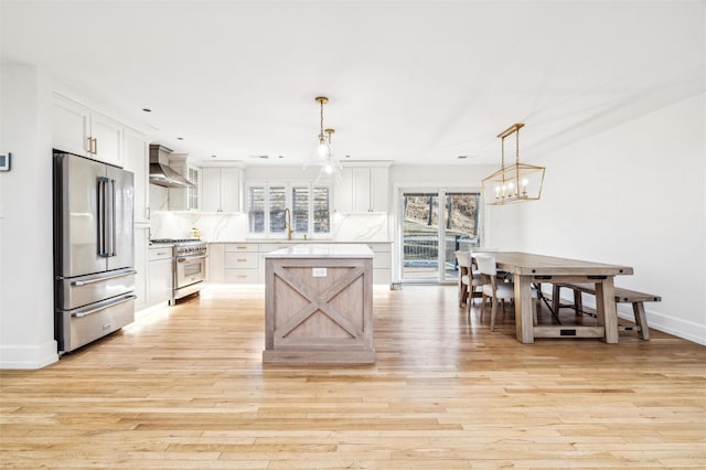 kitchen featuring white cabinetry, hanging light fixtures, high quality appliances, and wall chimney range hood