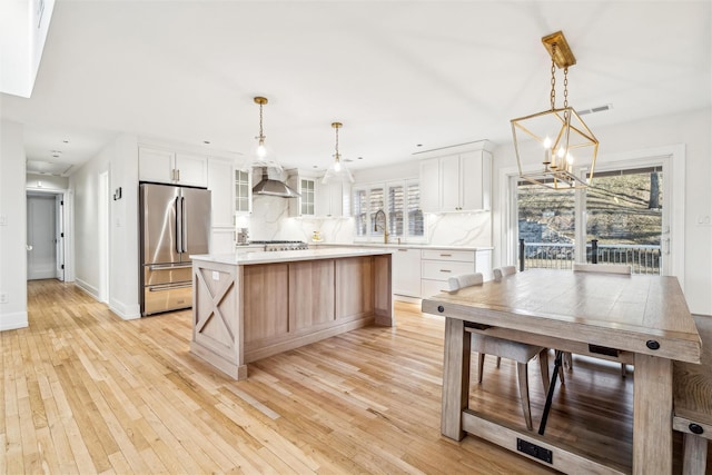 kitchen with wall chimney exhaust hood, stainless steel appliances, a kitchen island, tasteful backsplash, and white cabinets