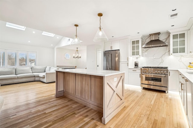 kitchen featuring premium appliances, a kitchen island, white cabinetry, and wall chimney range hood