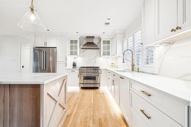 kitchen with decorative backsplash, wall chimney range hood, high quality appliances, white cabinets, and hanging light fixtures