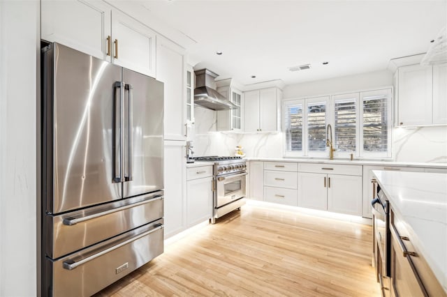 kitchen with light stone countertops, backsplash, premium appliances, wall chimney range hood, and white cabinetry