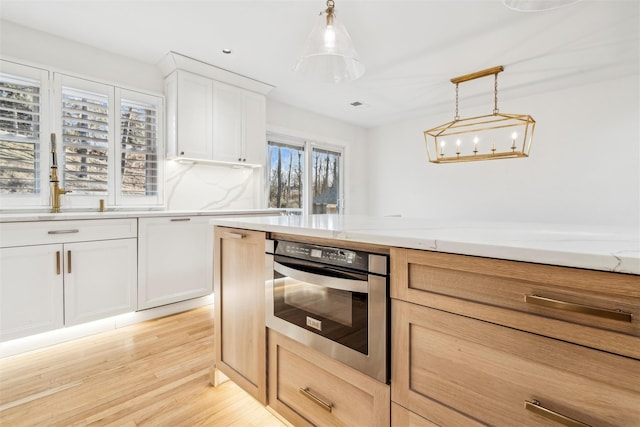 kitchen with light stone counters, light brown cabinets, oven, white cabinetry, and hanging light fixtures