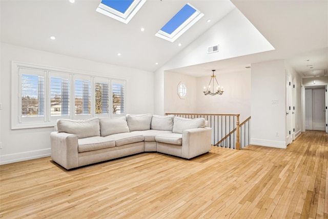 living room featuring a notable chandelier, light hardwood / wood-style floors, high vaulted ceiling, and a skylight