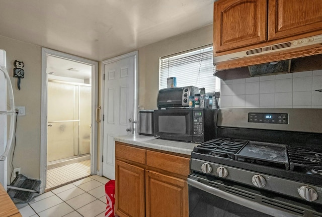 kitchen with light countertops, under cabinet range hood, stainless steel range with gas cooktop, black microwave, and backsplash