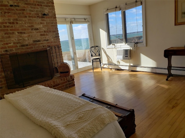 bedroom featuring a baseboard radiator, wood finished floors, a brick fireplace, and access to exterior