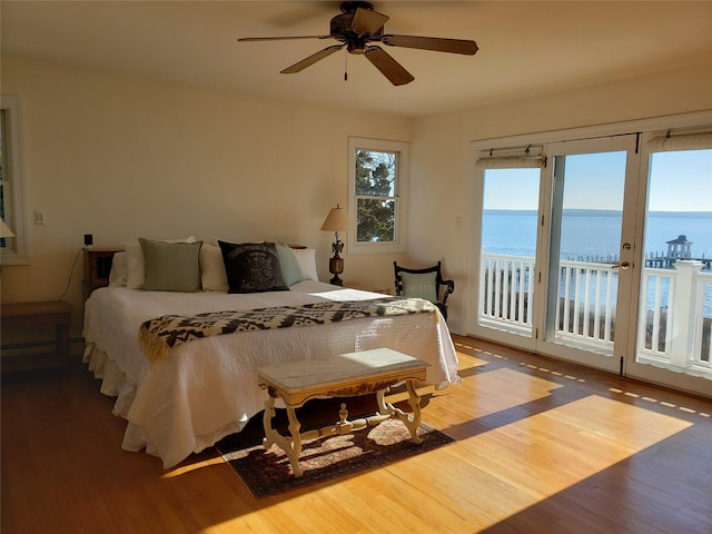 bedroom featuring wood finished floors, a water view, ceiling fan, and access to outside