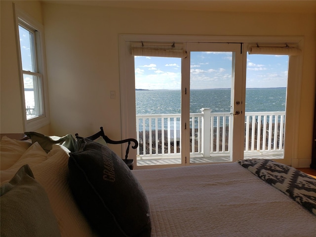 bedroom with multiple windows, access to exterior, a beach view, and a water view