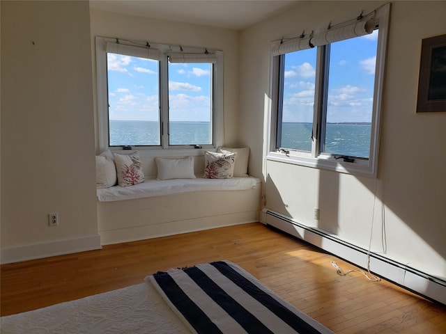 living area with baseboards, a baseboard heating unit, light wood-style floors, and a water view