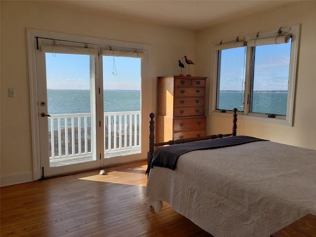 bedroom with access to exterior, a water view, and hardwood / wood-style floors