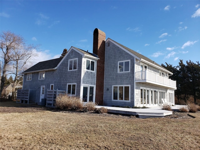 rear view of house featuring a balcony, a chimney, and a lawn