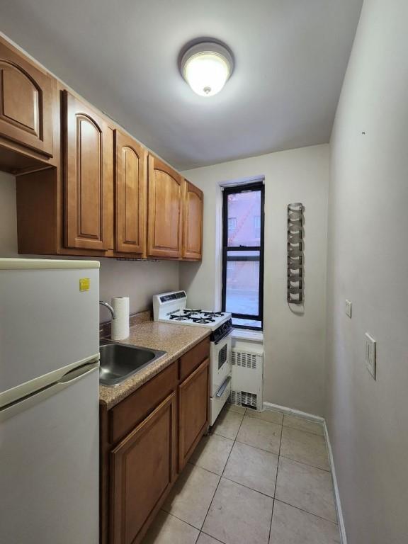 kitchen featuring sink, white appliances, radiator, and light tile patterned flooring