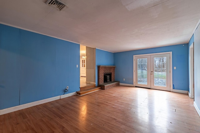 unfurnished living room with a brick fireplace, light wood-type flooring, and french doors