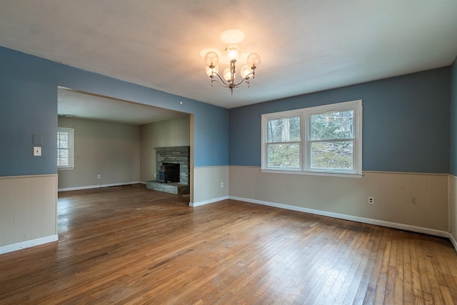 unfurnished living room with hardwood / wood-style floors, a stone fireplace, and a notable chandelier