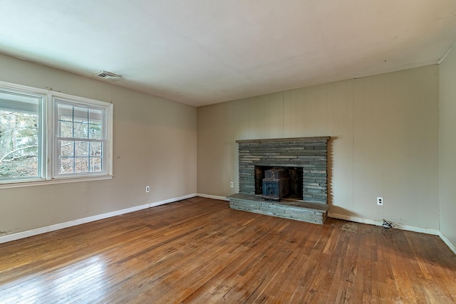 unfurnished living room with wood-type flooring and a stone fireplace