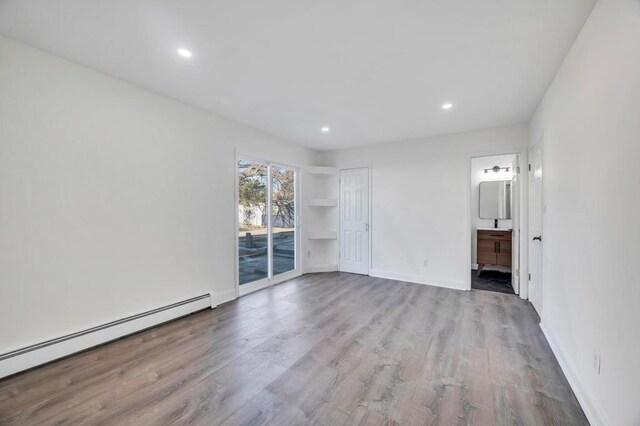 spare room with built in shelves, light wood-type flooring, and a baseboard radiator