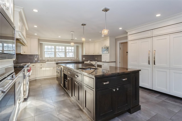 kitchen featuring sink, hanging light fixtures, stainless steel appliances, decorative backsplash, and a center island with sink