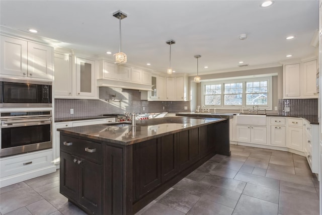 kitchen featuring a kitchen island with sink, white cabinets, oven, hanging light fixtures, and black microwave