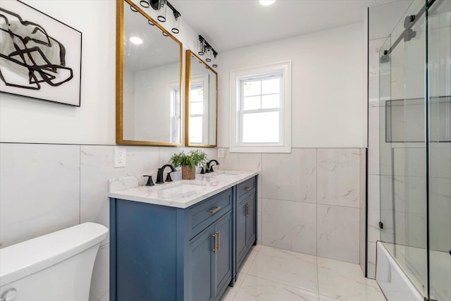 full bathroom with vanity, toilet, tile walls, and bath / shower combo with glass door