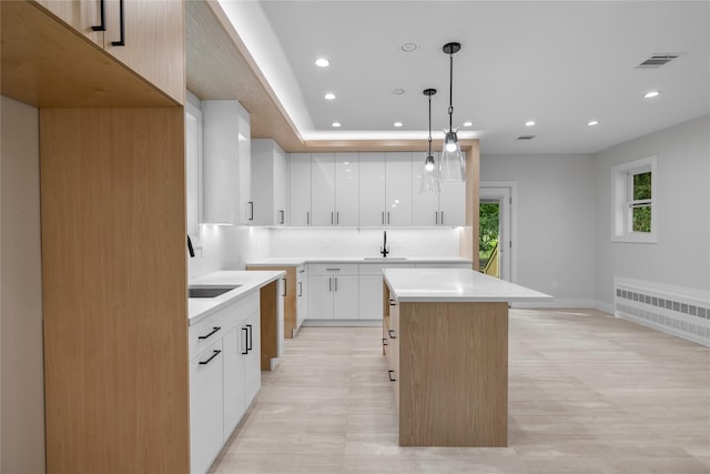 kitchen featuring white cabinets, sink, decorative light fixtures, a kitchen island, and radiator heating unit