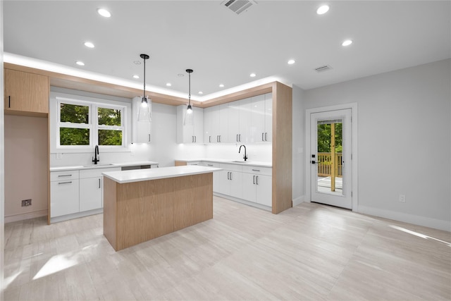 kitchen featuring decorative light fixtures, a kitchen island, white cabinetry, and sink