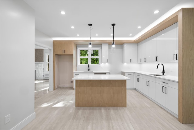 kitchen with a center island, white cabinets, sink, light wood-type flooring, and decorative light fixtures