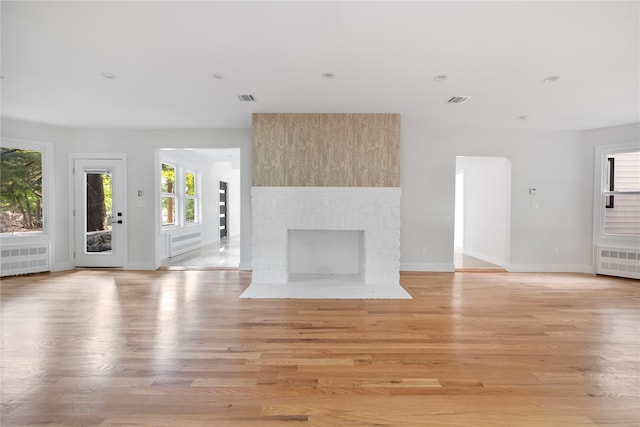 unfurnished living room with radiator, a fireplace, and light wood-type flooring