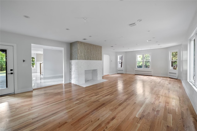 unfurnished living room featuring a fireplace, radiator heating unit, and light hardwood / wood-style floors