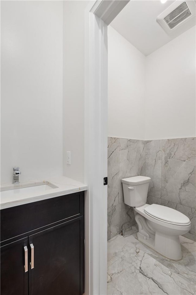 bathroom with vanity, toilet, and tile walls