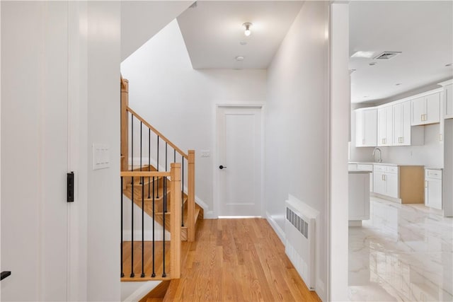 hall with radiator heating unit, light wood-type flooring, and sink